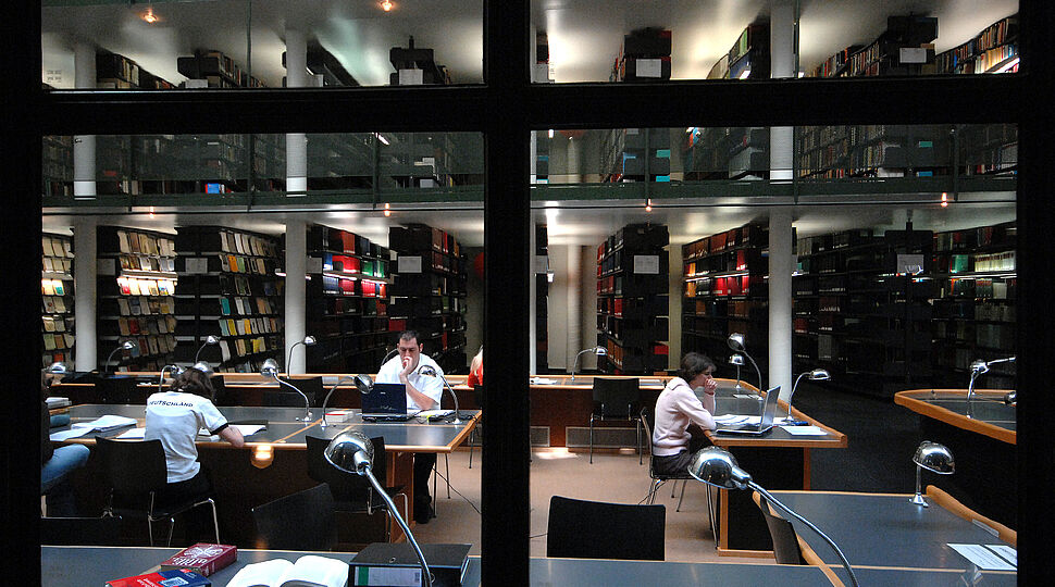 Blick durch das große Glasfenster in den Lesesaal, in dem Studierende lesen und arbeiten Bibliothek_KNA_185301.jpg