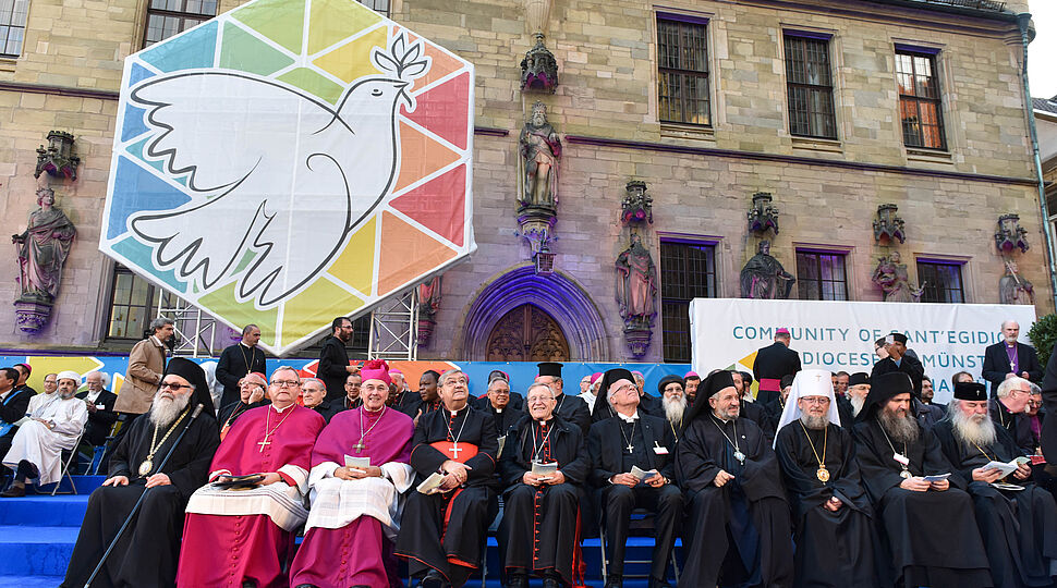 Gruppenfoto unter dem Tansparent einer Friedenstaube, Symbol des Heiligen Geistes Interreligioeser-Dialog-170912-93-000308.jpg