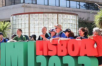 Pilger stehen hinter einem grün-roten menschenhohen Logo des Weltjugendtags "JMJ Lisboa 2023" am 1. August 2023 in Lissabon (Portugal).